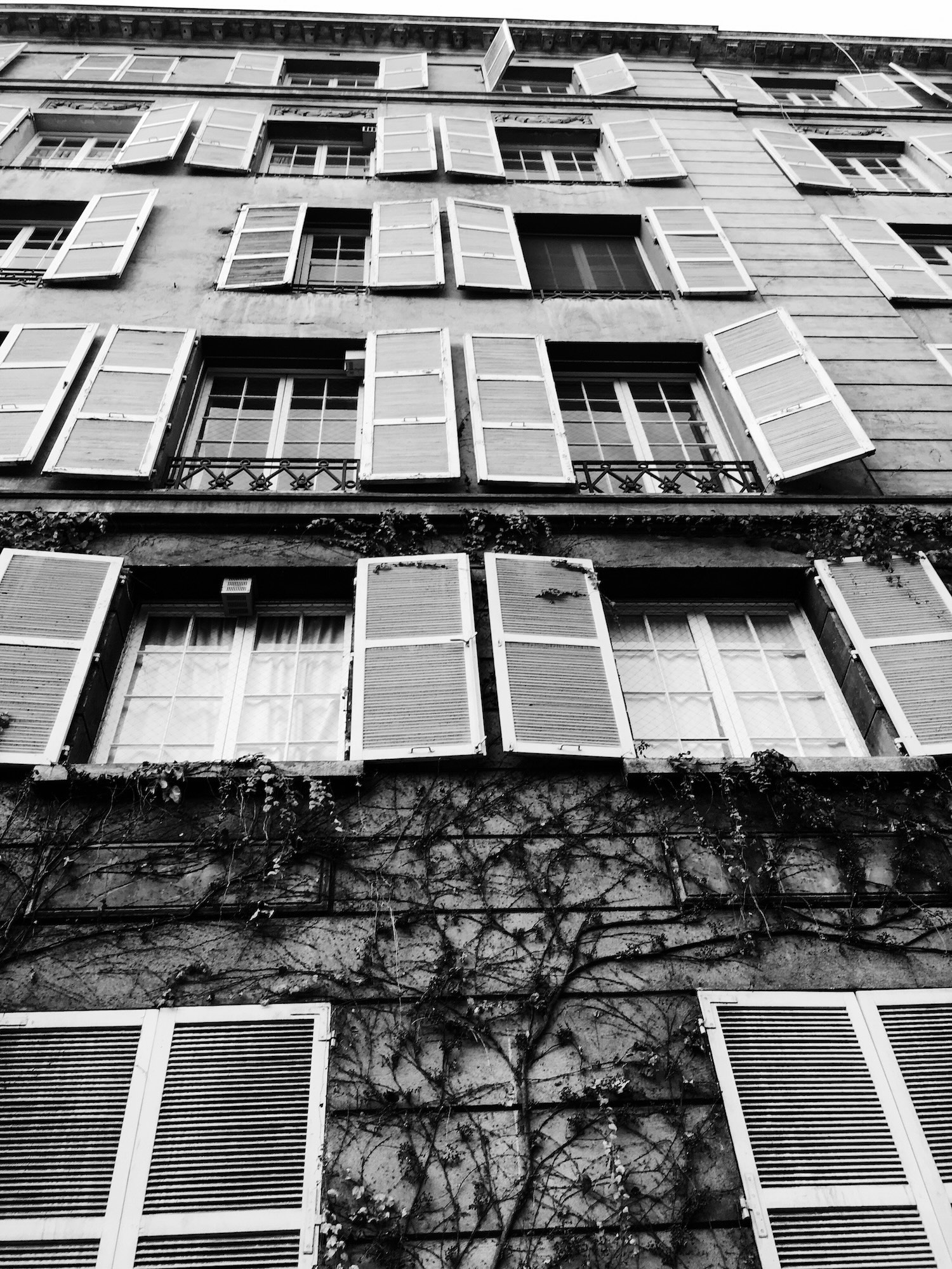 Looking up a six-floor building, with some wooden blinds open and a few ones closed, Santiago.