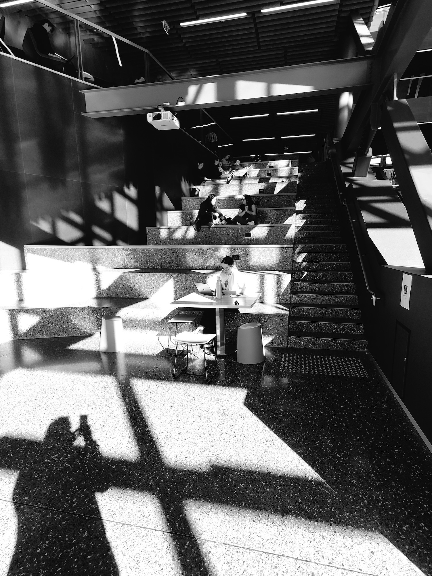 Photographer and window frames shadows darken a staircase where university students seat during break.