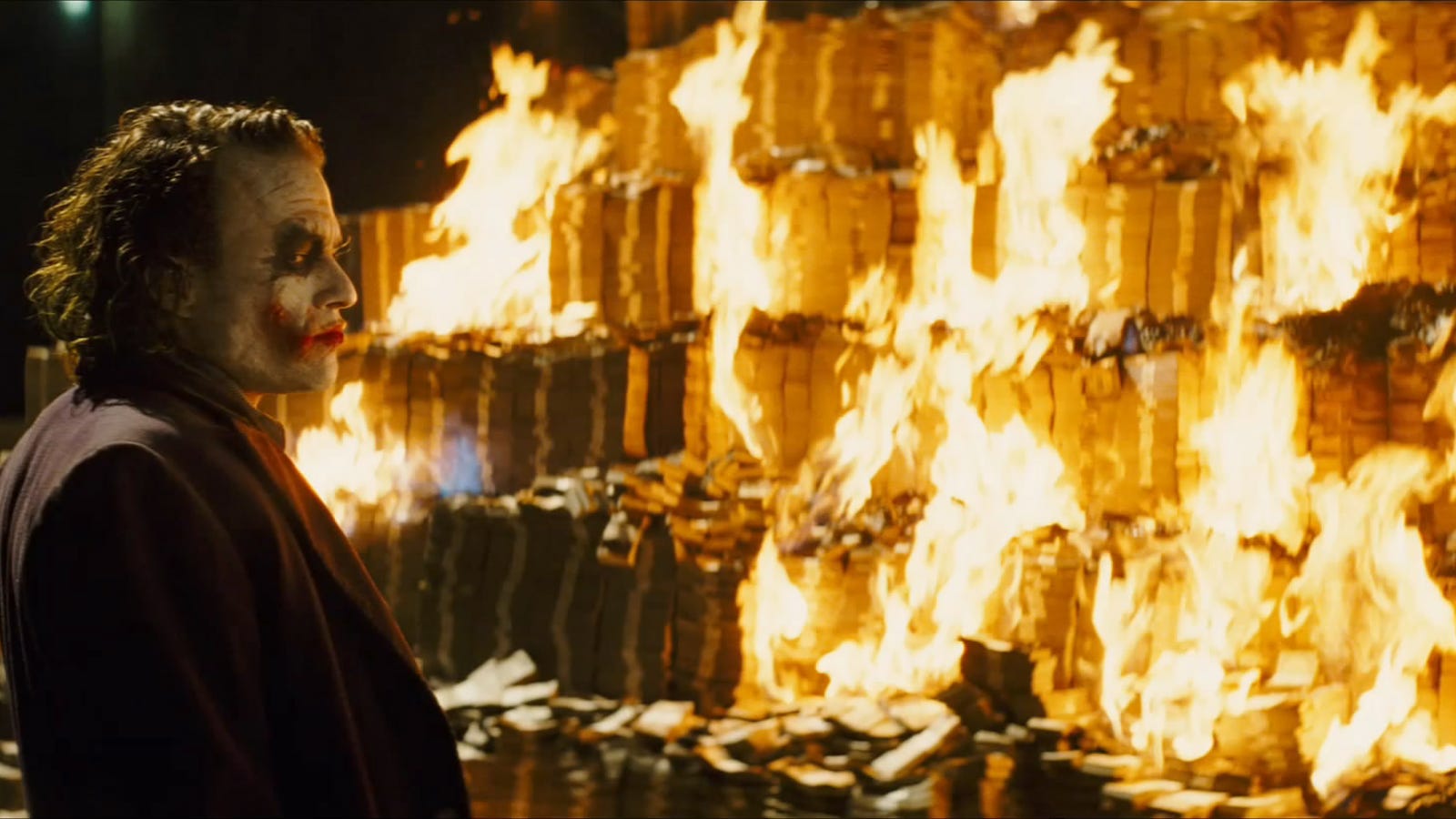 The Joker staring at piles of money burning.